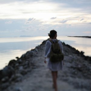 A woman walks on a rocky path by the tranquil seaside during twilight.